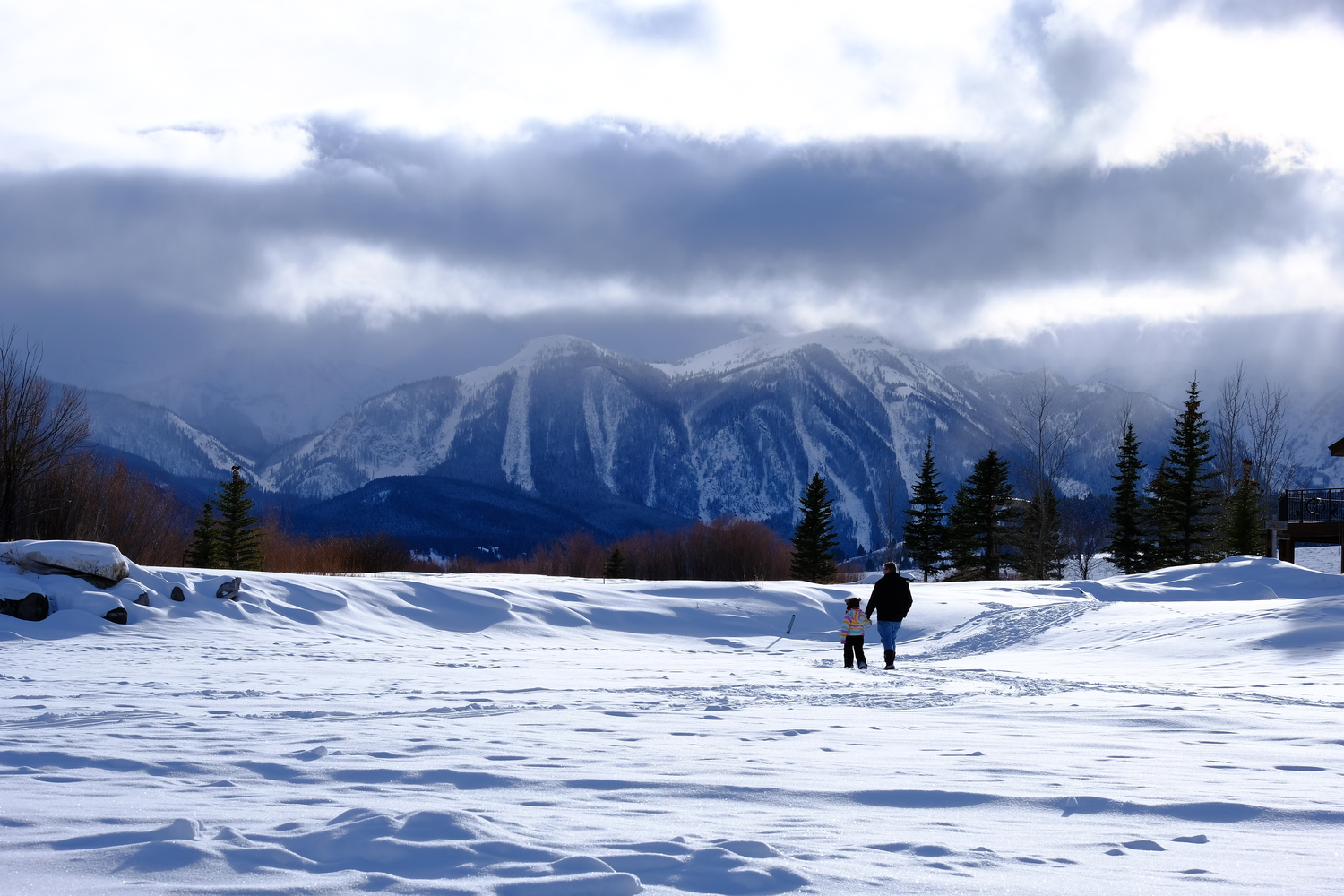 Photo of a father and daughter walking on the ice of Henry's Lake at winter time, in Island Park, Idaho. The backdrop is a gorgeous range of mountains covered in snow.