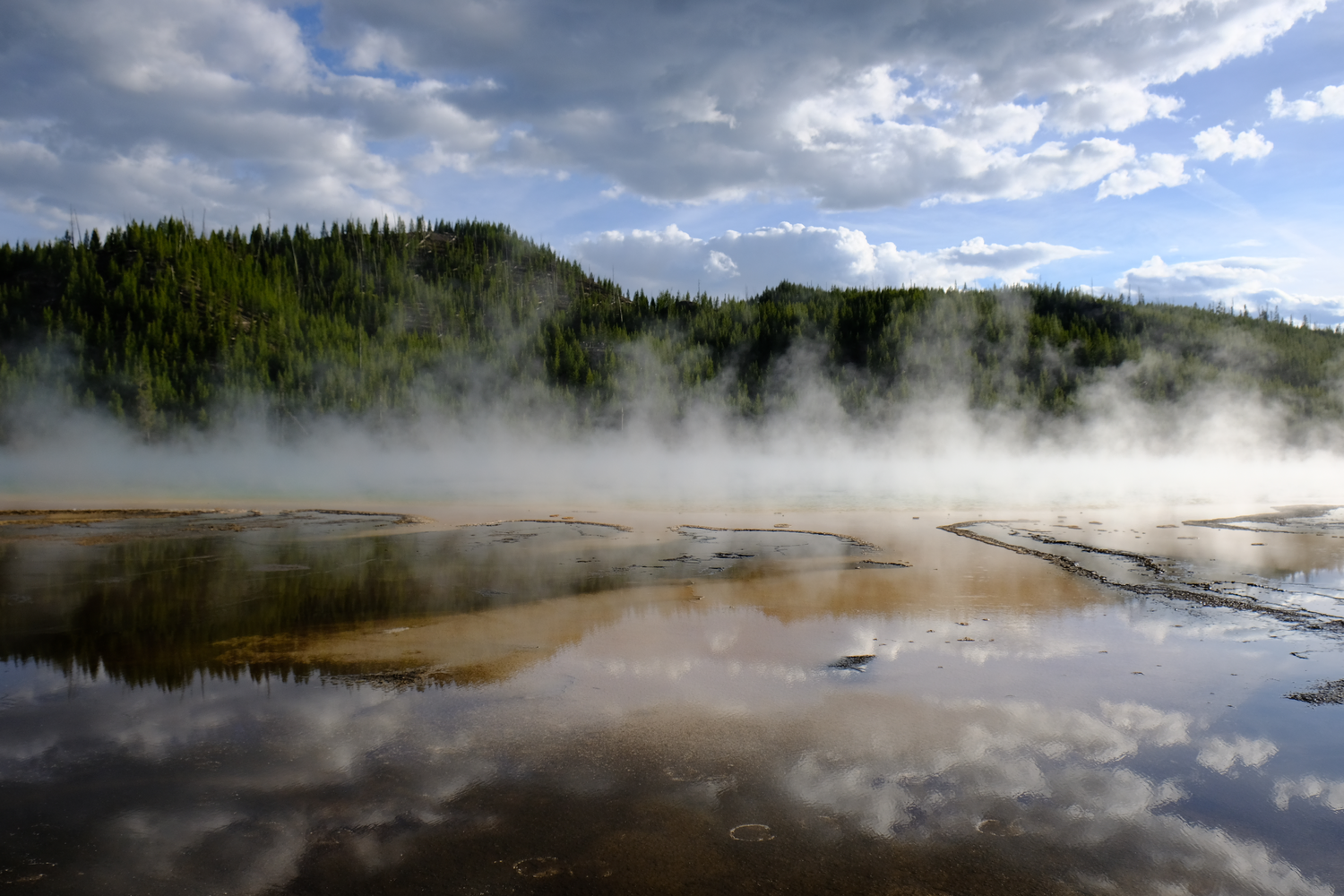 Photo of geyser water's reflection of the cloudy sky in Yellowstone National Park